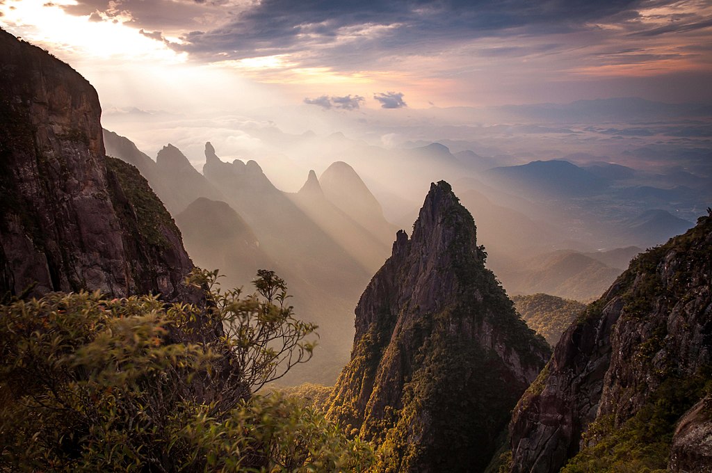 Jagged mountains surrounded by light fog are illuminated by sunlight.