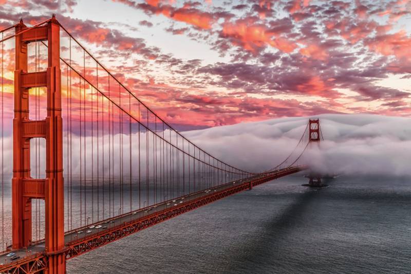 Golden Gate Bridge partially covered in fog with red clouds.