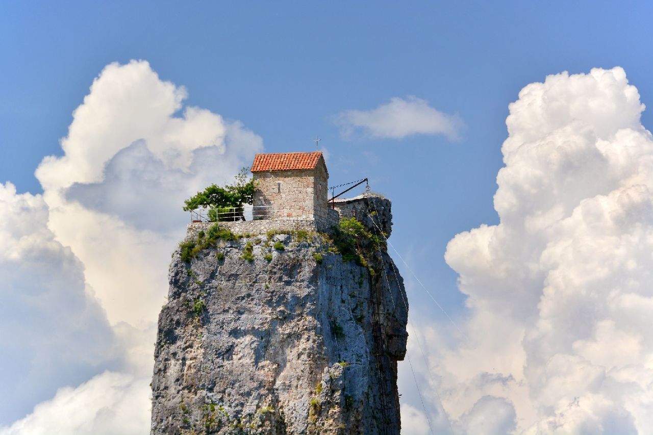 Small building on top of a tall, thin rock with large clouds in the background.