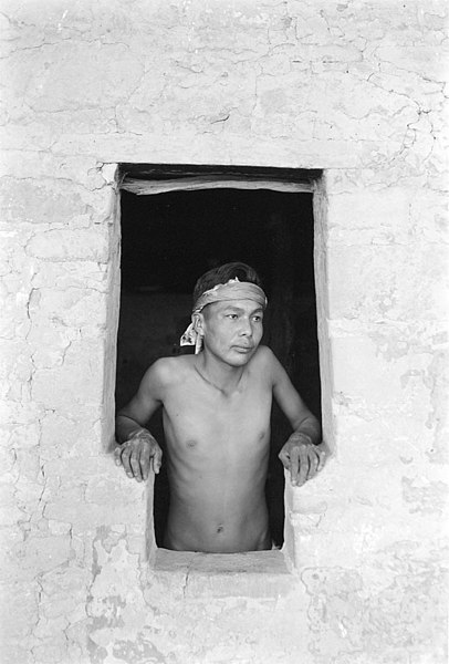 Native American man looks through a window in a pueblo.